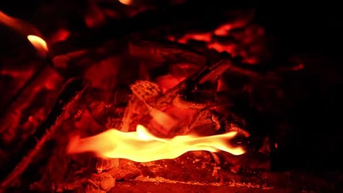 Burnt out campfire with hot red embers. Small flames appear on the charcoals. Close up.