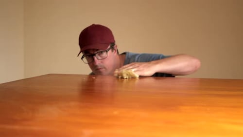 Man Cleans Wooden Table Surface in Home