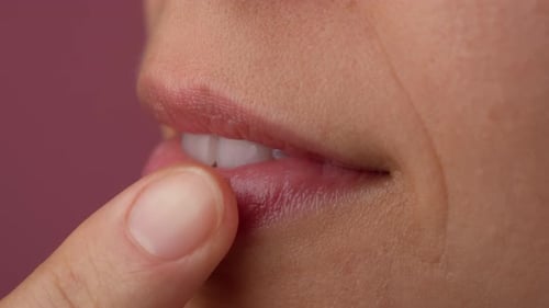 Nahaufnahme weiblicher rosafarbener Lippen, die Lippenbalsam mit dem Finger auftragen Makroaufnahme einer schönen kaukasischen Frau