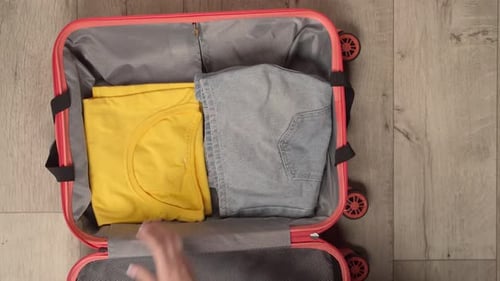 Woman's Hands Packing a Peachcolored Suitcase with Summer Clothing and Travel Essentials of Top View