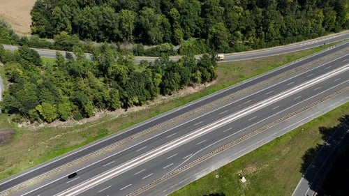 Traffic on highway with trucks on exit near green forest trees and farm fields. Sunny Day in