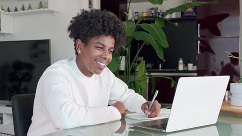 Young Adult Writing in Notebook While Using Laptop