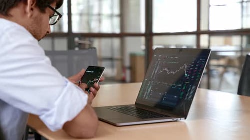 Indian trader analyzes stock market data on laptop and mobile app in his office