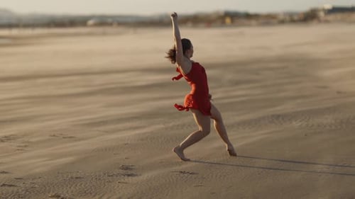 Graceful Young Woman in Red Dress Dancing on Sandy Beach