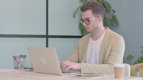 Excited Man Typing on Laptop in Modern Office
