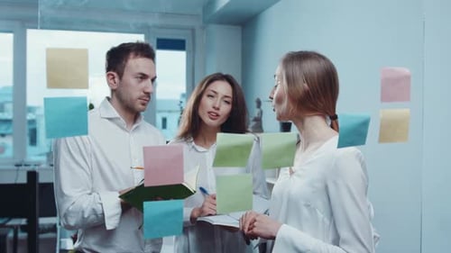 Jeune équipe joyeuse de trois travailleurs réfléchissant au projet en prenant des notes sur des autocollants colorés