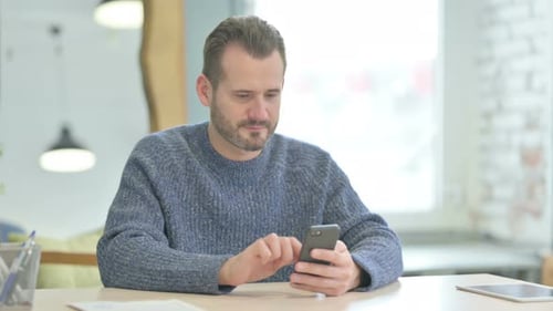 Middle Aged Man Browsing Internet on Smartphone in Office