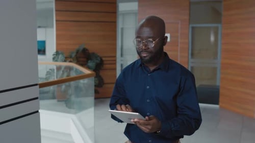 African American Office Worker Using Tablet while Walking in Hall