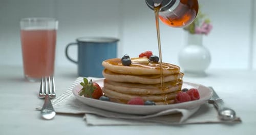Bottle of Maple Syrup Being Poured Over a Stack of Delicious Plate