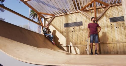 Video of happy diverse female and male skateboarders training in skate park