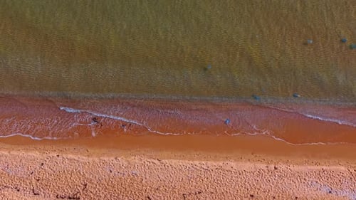 Flight over the sandy shore of the sea. Little waves splash to the beachline.
