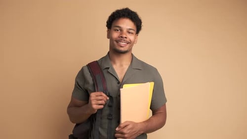 Happy Male University Student with Backpack and Books in Beige Studio