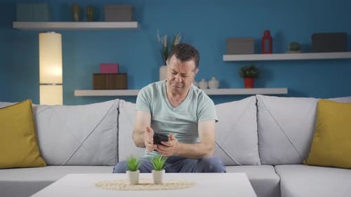 Distressed Man Uses Mobile Phone on Couch at Home