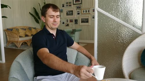 Man Sits and Drinks Coffee in Armchair