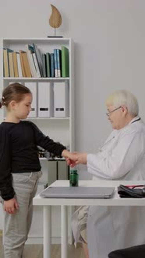 Vertical Screen Doctor pediatrician speaks caringly to a school girl in private clinic office.