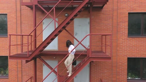 Woman Walking Down Metal Staircase on Brick Building