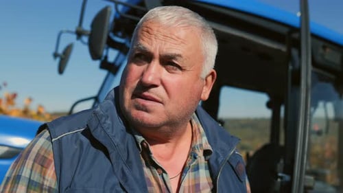 Farmer Standing Near a Blue Tractor on a Sunny Day