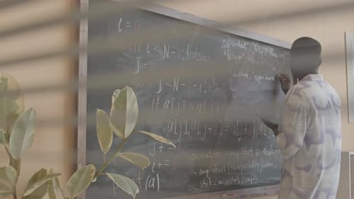 Adult Writes on Chalkboard Covered in Formulas