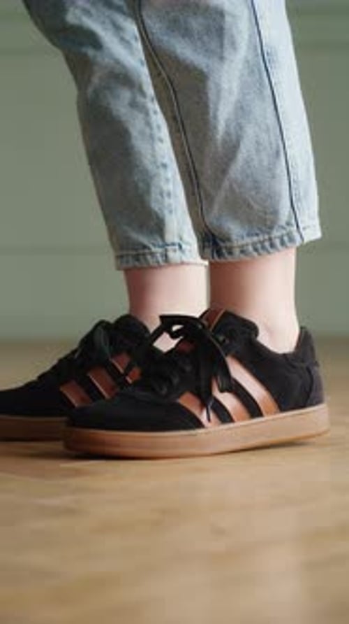Side View of a Person Wearing Black and Brown Sneakers with Rolledup Blue Jeans Indoor Lifestyle