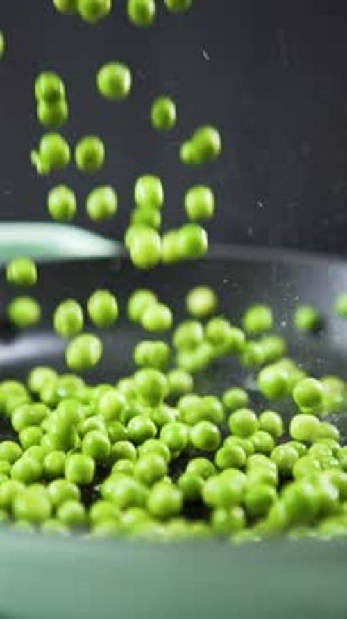 Vertical shot of Green peas falling in slow motion into a sizzling hot frying pan.