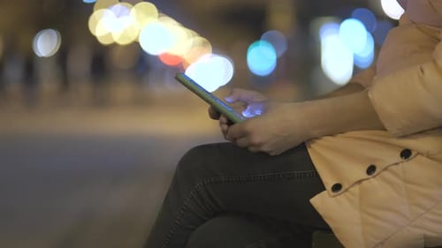 Closeup of Female Hands Holding Mobile Phone Browsing Internet on City Street with Blurred Lights at