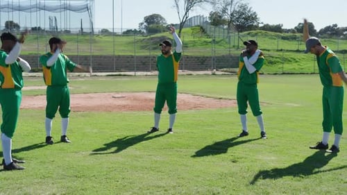 Raising right arms, male teammates warming up with arm stretches on outfield, with gloves, caps