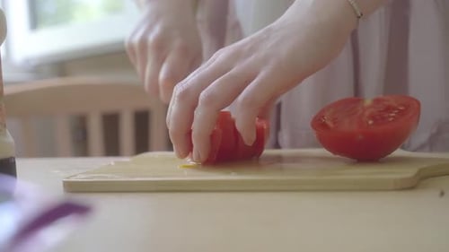 Slicing and preparing red tomatoes in the kitchen. Young woman preparing food. Close-up of hands