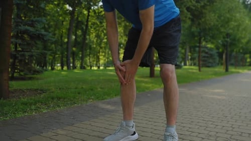 Closeup of Athletic Fit Mature Man Jogger Massaging Injured Knee During Run