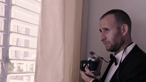 Man spying from a window and taking pictures. photographer in a black suit smiling and having fun st