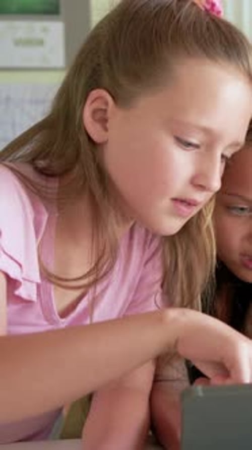Vertical video: Leaning in, tapping student in pink top using tablet while working at desk, poster