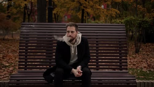 man smokes an electronic cigarette in the park sitting on a bench - spring