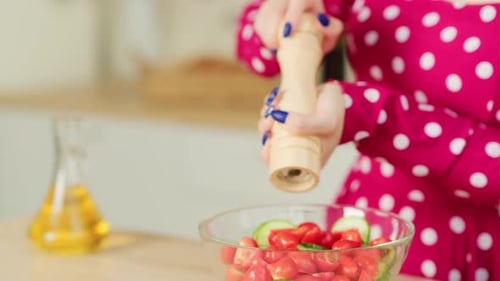 Femme méconnaissable poivrant une salade de légumes dans la cuisine