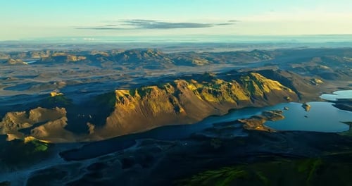 Aerial golden-hour view of Iceland highlands volcanic ridge above a winding lake, sunlit peaks and