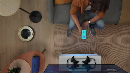 Top View Close Up Shot of Man Sitting on the Couch Switching on House Gadgets By App on Smartphone