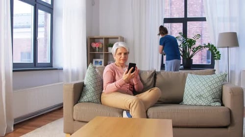 Senior Woman Using Phone While Woman Cleans Window