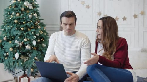 Couple using laptop with Christmas tree in background