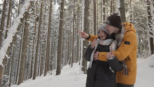 A Couple in Love Enjoying the Winter Beautiful Scenery During a Romantic Walk in the Woods He Points