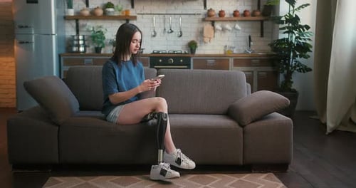 Woman with Disability Sits on Sofa Typing Messages on Phone