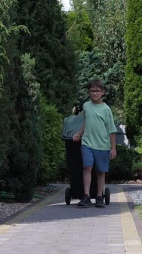 Vertical Video Boy Dragging a Garbage Can on Wheels Garbage Disposal