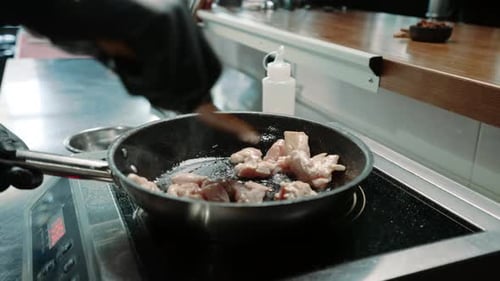 chef in a professional kitchen in a restaurant frying juicy chicken fillet in a pan close-up