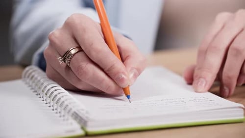 Young Woman Works Holds a Pen in Her Hands and Makes Notes in a Notebook While Sitting at a Table