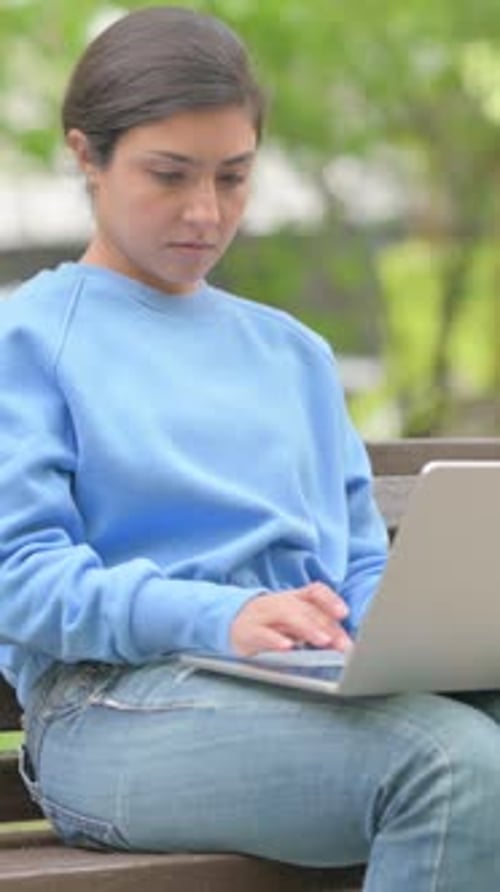 Woman Uses Laptop on Bench in an Urban Park