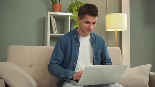 Young Man Works on Laptop at Home on Couch