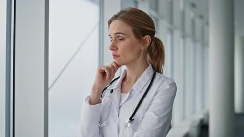 Nachdenklicher Praktiker, der ein Problem hat, steht am Krankenhausfenster, Nahaufnahme