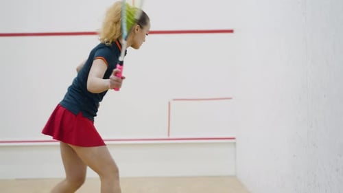 Professional Lady Squash Player Hits Ball Against White Wall