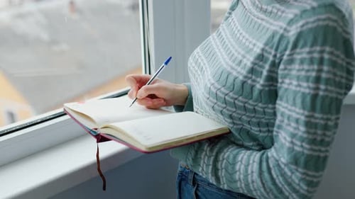 Woman Writing in Notebook by Window
