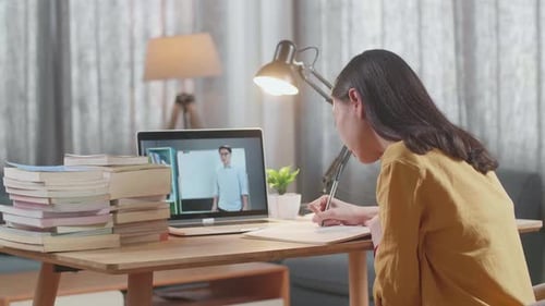 Side View Of A Young Female Looking At A Male Teacher Teaching On A Laptop While Studying At Home