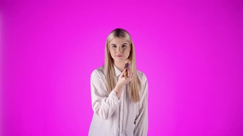 Feminin young woman applies makeup on face, cosmetic brush, purple background