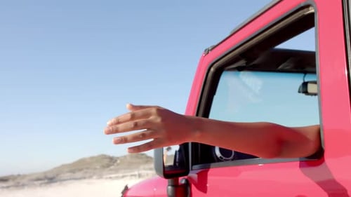 O braço de uma pessoa se estende de um veículo vermelho em uma viagem, sinalizando para o exterior