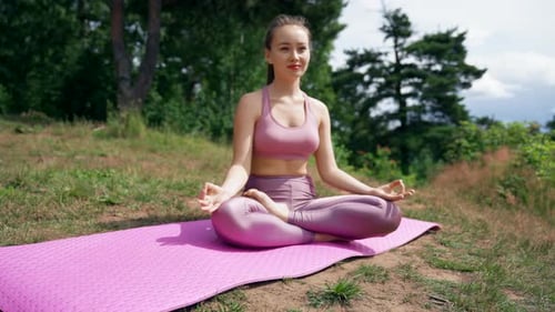 Smiling Woman Meditates on Mat in Lotus Pose on Meadow